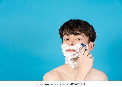 Portrait Of Teenager Boy Shaving Face Isolated On Blue Background.