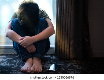 Portrait of a teenager boy sitting alone in the room with his smartphone, feeling hurt, anxiety and depress from Cyber bullies on social media. Technology cause teens mental health problems concept.