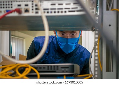 Portrait Of A Teenager In A Data Center.A Technician In A Medical Mask Works In A Rack With Computer Equipment. The Man Serves The Server Room In The Datacenter.