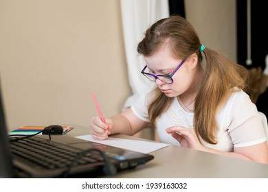 Portrait Of Teenager Girl With Down Syndrome Learning Online At Home. Distance Learning By Video Call On Laptop. E-learning And Online Education For Kids With Special Needs Concept