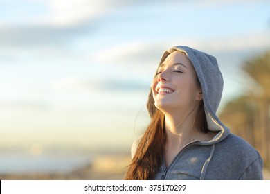 Portrait of a teenager girl wearing hood breathing deep fresh air on the beach at sunrise in a summer sunny day with a beautiful warm sky in the background