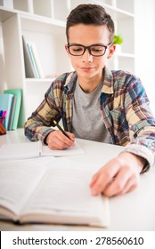 Portrait of teenager  in glasses sitting at the table and doing homework at home.
