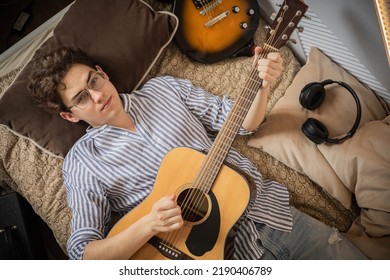 Portrait Teenager Man Playing Acoustic Guitar Lying On Comfy Bed Relaxing Enjoy Art Entertainment Hobby Top View. Male Guitarist Musician Player Singing Song Music Instrument Resting At Home