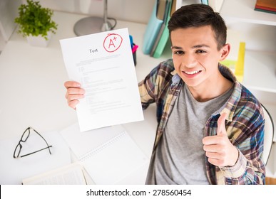 Portrait of teenager sitting at the table at home and showing perfect test results.