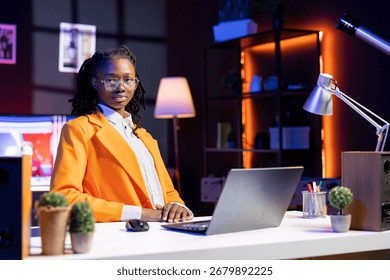 Portrait of teleworker crosschecking analytics statistical data on laptop, remotely working in dimly lit apartment office. Freelancer optimizing key performance indicators teleworker using notebook