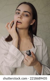 Portrait Of Tender Young Woman Applying Protective Lip Balm With Finger While Doing Skin Care Beauty Routine And Looking At Camera At Home 