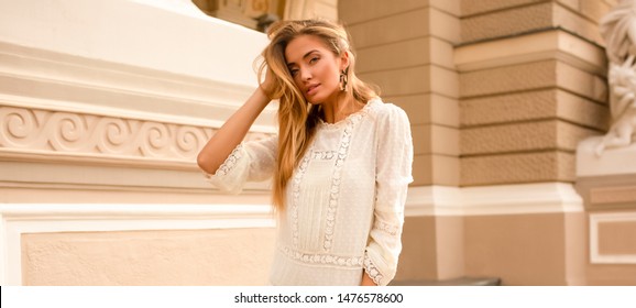 Portrait Of A Tender Young Woman With Blonde Volume Hair, Soft Tanned Skin And Slim Body. Wearing White Dress With Sleeves, Accessories. Makeup On The Face, Big Lips. Sexy Summer Look