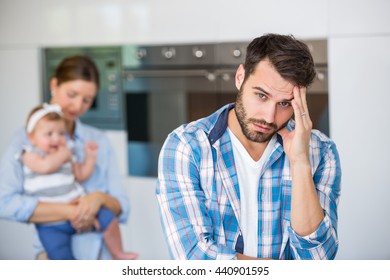 Portrait of tensed man with wife carrying baby in background at home - Powered by Shutterstock