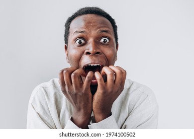 Portrait of a terrified African man staring in horror at the camera and putting his hands to his mouth in a light linen shirt on a white background. Very strong surprise or fright, horror in the eyes.
