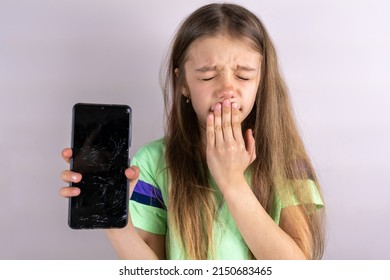 Portrait Of Terrified Child With Damaged Phone. Upset Little Girl Breaks Screen Of Mobile Phone. Kid Girl Holding Broken Display. Worried Child Accidentally Destroyed Smartphone