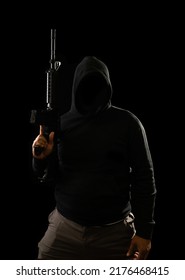 Portrait of a terrorist wearing a black hoodie holding a m16 rifle on a black background.concept of terrorism.