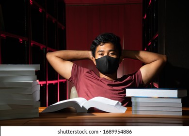 Portrait Of Thai Asian Black Man Short Hair Wearing Mask And Red Shirt Relax With A Lot Of Book In Library Stock Photo