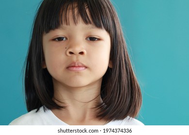 Portrait Of Thai Asian Kid Girl With Cute Face, Long Hair, Sad Face, Not Smiling, Showing Thinking. Her Mood Is Not Very Good. Healthy And Good Personality, Ages 4 To 6, Green Background. 