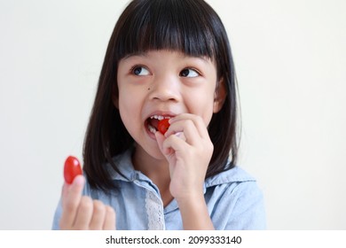 Portrait Of A Thai Asian Kid Girl, Aged 4 To 6 Years Old, Cute And Bright. She Is Smiling, In Her Hand The Fruit Of A Tomato. She Eats Fruit Make Good Health Happy Face. Isolate White Background