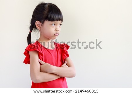 portrait of Thai Asian kid girl, age 4 to 6 years old, cute face, long hair. wearing a red shirt She stood with her arms crossed. looking sideways sad face scowling bad mood, isolated white background
