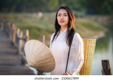 Portrait of Thai girls with Ao Dai, Vietnam traditional dress holding a hat and standing on wooden bridge looking the other way.