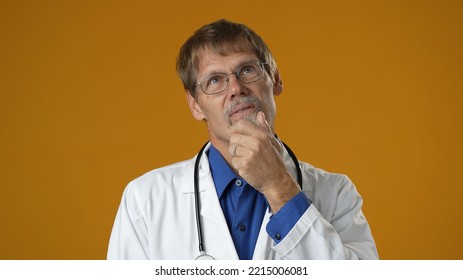 Portrait Of Thinking Pondering Doctor Man In Medical Coat Having Idea Moment On Solid Yellow Studio Background. Smiling Happy Doc Showing Eureka