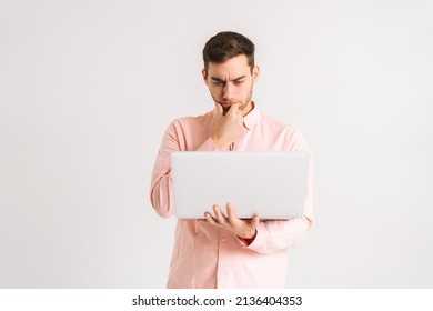 Portrait of thinking young man standing with laptop loiking on screen with confused puzzled face on white isolated background. Studio shot of pensive male posing with pc looking at screen - Shutterstock ID 2136404353