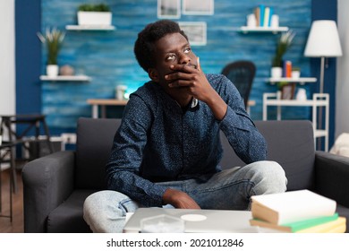 Portrait Of Thoughtful African American Man Looking Out The Window, Thinking About Workplace Business Problems. Black Adult Sitting In Living Room On Couch Working From Home Office