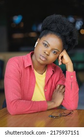 Portrait Of A Thoughtful African American Woman In A Pink Shirt And Glasses. A Happy Woman Is Relaxing In A Public Place And Posing. Selective Focus, Successful Confident Millennial Woman Smiles. A