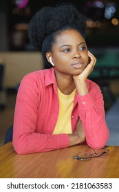 Portrait Of A Thoughtful African American Woman In A Pink Shirt And Glasses. A Happy Woman Is Relaxing In A Public Place And Posing. Selective Focus, Successful Confident Millennial Woman Smiles. A