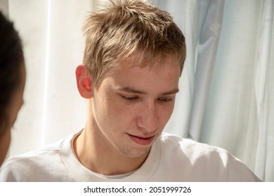 Portrait Of A Thoughtful Guy 20-25 Years Old In The Kitchen By The Window, Next To A Woman. Concept: A Serious Conversation With The Mother, A Conversation With A Psychologist, Ashamed Of Misconduct.