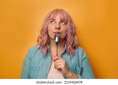 Portrait Of Thoughtful Hungry Woman Holding Spoon Isolated Over Yellow Wall Background. Health Care Concept