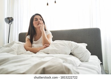 Portrait of a thoughtful lady with loose dark hair sitting in bed in the morning - Powered by Shutterstock