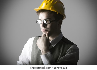 Portrait of thoughtful smart young engineer with helmet against grey background - Shutterstock ID 187595633