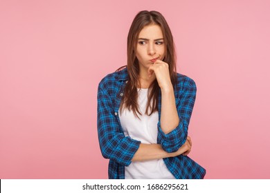 Portrait of thoughtful upset girl in checkered shirt pondering serious issues, looking with uncertain hesitant expression, making difficult choice. indoor studio shot isolated on pink background