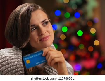 Portrait Of Thoughtful Woman With Credit Card In Front Of Christmas Lights