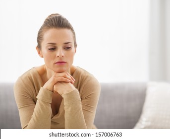 Portrait of thoughtful young housewife sitting on couch