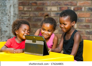 Portrait of three African girls playing leisure games on tablet.