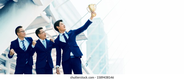 Portrait Of Three Asian Businessmen Wearing A Blue Suit Standing With A Trophy Obtained From Successful Work From Teamwork And Honesty. Developing Company Personnel To Excel And With Modern Knowledge