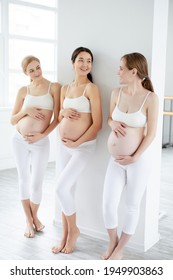 Portrait of three attractive young pregnant women standing in studio in white sportive outfit