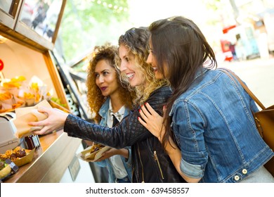 Portrait of three beautiful young women visiting eat market in the street.