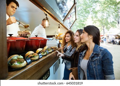 Portrait of three beautiful young women buying meatballs on a food truck in the park.