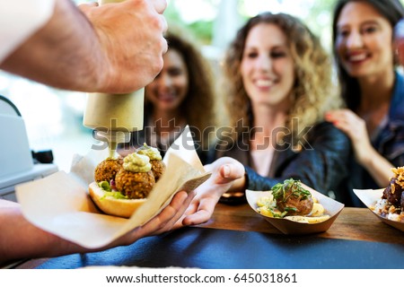 Portrait of three beautiful young women buying meatballs on a food truck in the park.