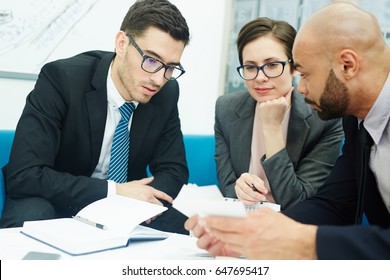 Portrait Of Three Business People Sitting At Round Table In Meeting, Discussing Work