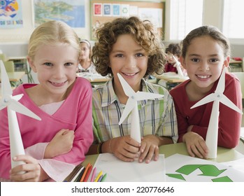 Portrait Of Three Children Looking To Camera With Paper Windmills Illustrating Alternative Energy In A School Classroom