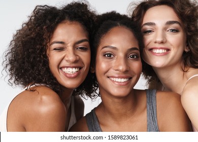 Portrait of three delighted multiracial women standing together and smiling at camera isolated over white background - Shutterstock ID 1589823061