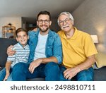 Portrait of a three generation family, male part, grandfather, parent father and children son sitting on sofa and having fun posing at home