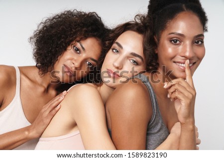 Portrait of three gorgeous multiethnic women showing shh finger while hugging together isolated over white background