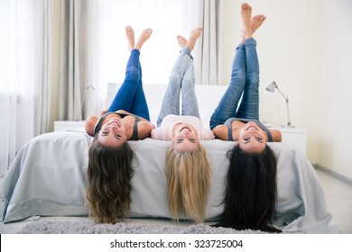 Portrait of a three happy girls lying on the bed wth raised legs and looking at camera at home