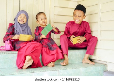 Portrait Of Three Kids, Happy Siblings Received Money Pocket Or Known As Duit Raya During Hari Raya Puasa Or Eid Mubarak Celebration. Muslim In Malaysian Celebrate Eid With Visiting Each Other.