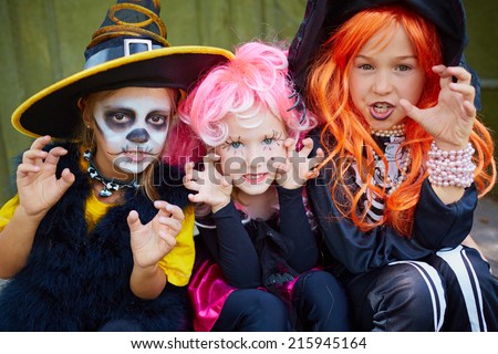 Portrait of three little girls in Halloween costumes looking at camera with frightening gesture