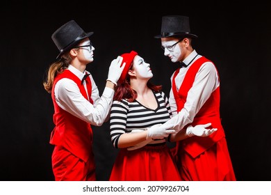 Portrait of three mime artists, isolated on black background. A man joins the heads of a man and a woman in a kiss. Symbol of procurement, Cupid, matchmaker