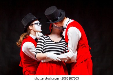 Portrait of three mime artists, isolated on black background. A man joins the heads of a man and a woman in a kiss. Symbol of procurement, Cupid, matchmaker