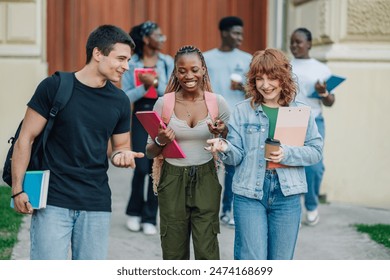 Portrait of three multicultural happy college students walking towards camera with textbooks and backpacks near university building entrance. Group of interracial students exiting university building. - Powered by Shutterstock