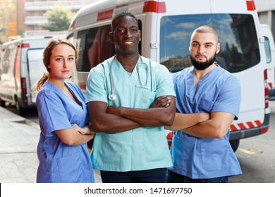 Portrait of three professional paramedicals in uniform near ambulance car outdoor